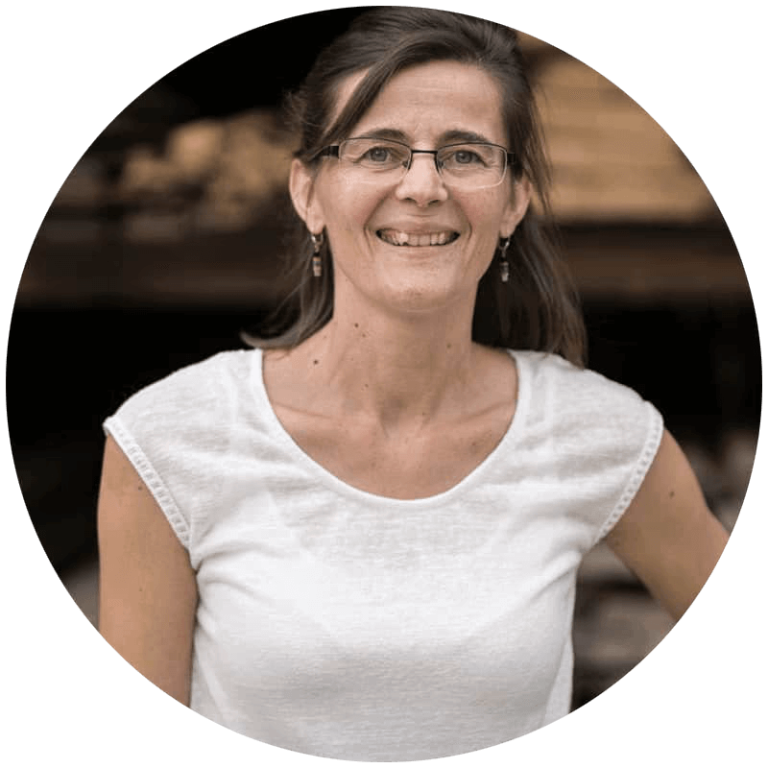 Lächelnde Frau in T-Shirt vor Holzwerkstätte, repräsentiert Holzbau Bachmaier in Neukirchen.